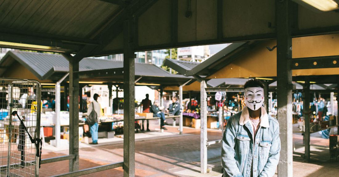 Local Policies - Unrecognizable black man in stylish clothes and Anonymous mask standing in local market in city and looking at camera in sunny day
