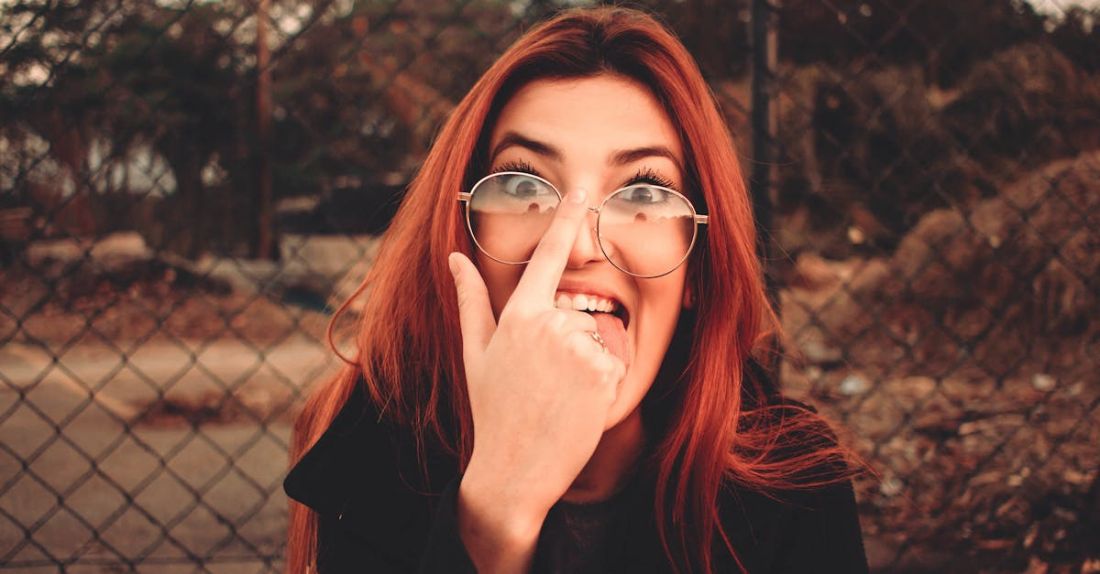 Smart Grids - Young playful female in eyewear with red hair making face and sticking tongue out while fixing glasses looking at camera on street